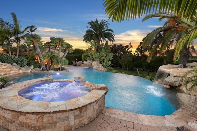 pool at dusk featuring pool water feature and an in ground hot tub