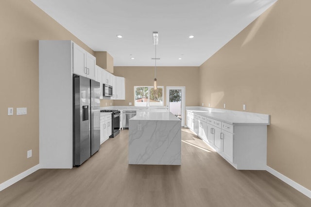 kitchen featuring white cabinetry, hanging light fixtures, stainless steel appliances, a kitchen island, and light wood-type flooring