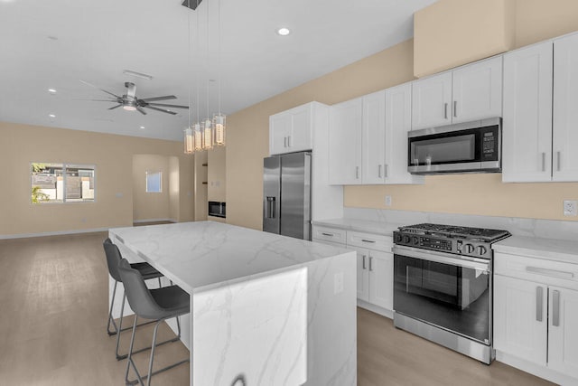 kitchen featuring appliances with stainless steel finishes, light hardwood / wood-style flooring, a center island, white cabinetry, and hanging light fixtures