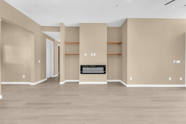 unfurnished living room featuring built in shelves and light wood-type flooring