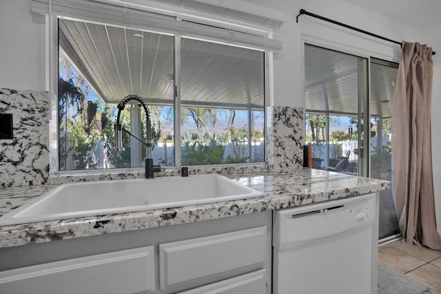 kitchen with white cabinets, sink, white dishwasher, and light tile patterned flooring