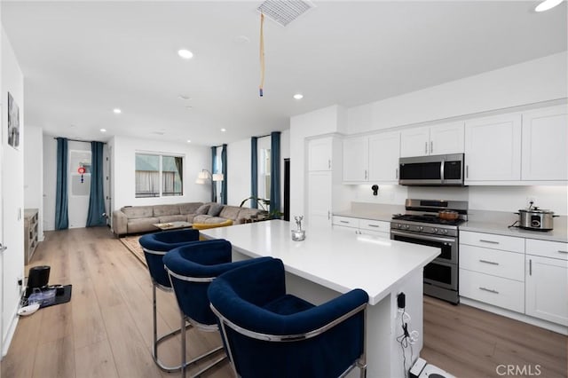 kitchen featuring appliances with stainless steel finishes, a breakfast bar, a kitchen island, light hardwood / wood-style flooring, and white cabinetry