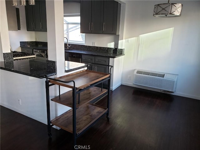 kitchen with dishwasher, dark hardwood / wood-style floors, a wall unit AC, dark stone counters, and pendant lighting