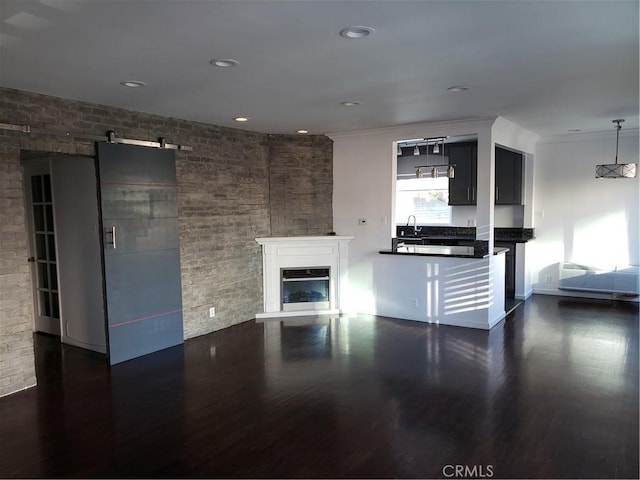 unfurnished living room with a barn door, crown molding, dark wood-type flooring, and brick wall