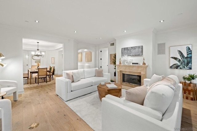 living room featuring light hardwood / wood-style floors, an inviting chandelier, ornamental molding, and a premium fireplace