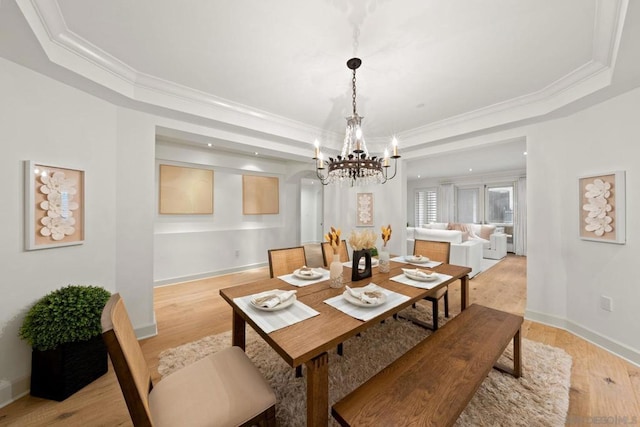 dining space with a raised ceiling, light hardwood / wood-style floors, and an inviting chandelier