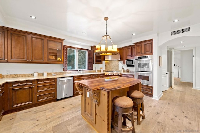 kitchen featuring a center island, stainless steel appliances, decorative light fixtures, and light wood-type flooring