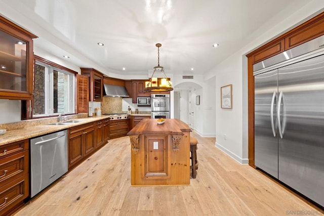 kitchen featuring a center island, light hardwood / wood-style flooring, wall chimney exhaust hood, appliances with stainless steel finishes, and decorative light fixtures