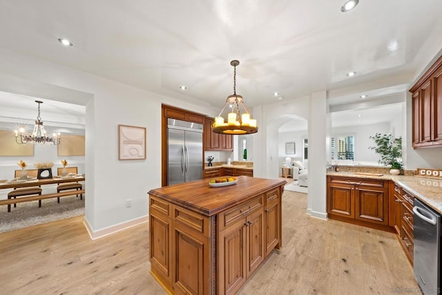 kitchen featuring light stone countertops, hanging light fixtures, stainless steel appliances, and light hardwood / wood-style floors