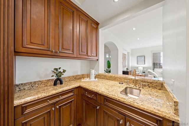 kitchen with kitchen peninsula, light stone countertops, and sink