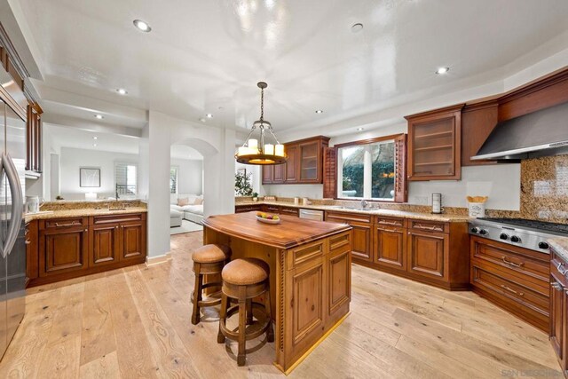 kitchen with appliances with stainless steel finishes, light stone counters, decorative light fixtures, light hardwood / wood-style flooring, and a center island