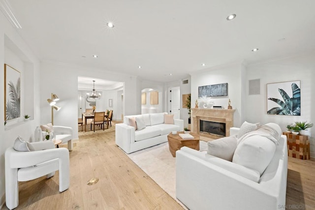 living room with light wood-type flooring, crown molding, and a chandelier