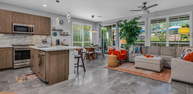 kitchen featuring sink, hanging light fixtures, stainless steel appliances, a kitchen bar, and a center island with sink