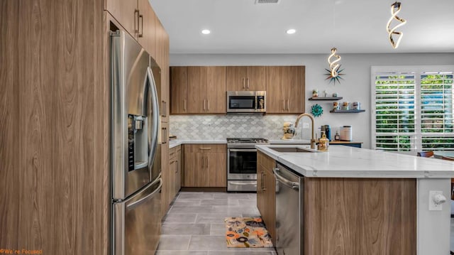 kitchen featuring tasteful backsplash, light stone counters, stainless steel appliances, sink, and an island with sink