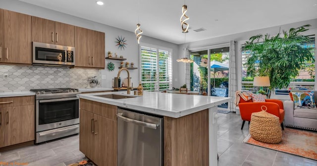 kitchen featuring pendant lighting, backsplash, a center island with sink, sink, and stainless steel appliances