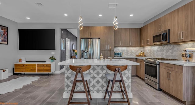 kitchen featuring sink, stainless steel appliances, decorative light fixtures, a kitchen bar, and a kitchen island with sink