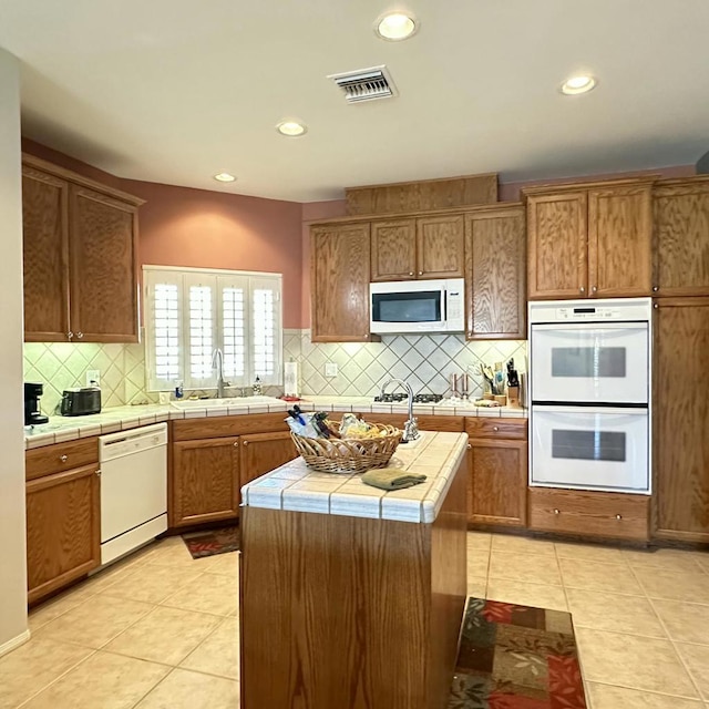 kitchen featuring tile countertops, a center island, white appliances, sink, and light tile patterned floors