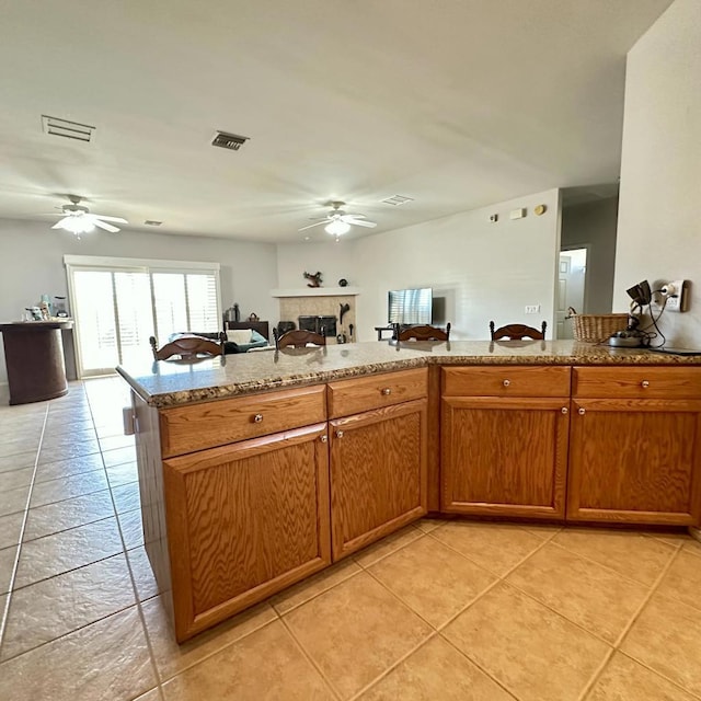 kitchen featuring ceiling fan, light tile patterned flooring, and light stone counters