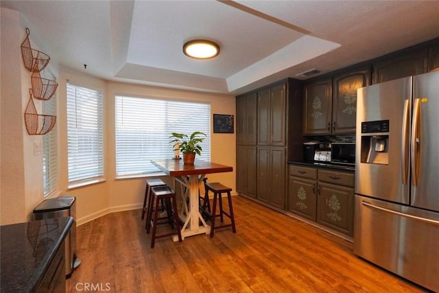 kitchen with a tray ceiling, dark brown cabinetry, wood-type flooring, and stainless steel refrigerator with ice dispenser