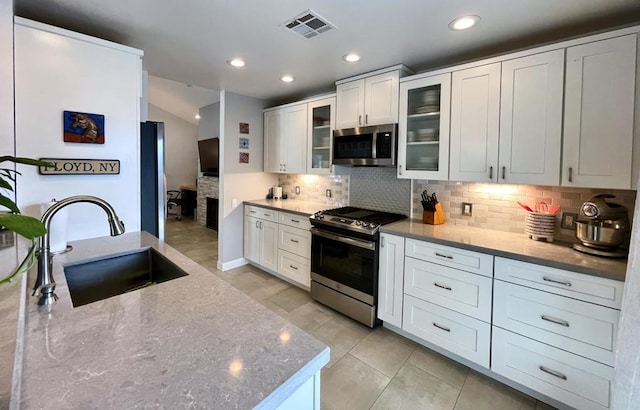 kitchen with white cabinetry, stainless steel appliances, decorative backsplash, light stone countertops, and sink