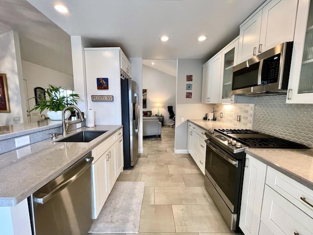 kitchen with appliances with stainless steel finishes, decorative backsplash, white cabinets, light stone counters, and sink