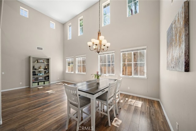 dining area with dark hardwood / wood-style flooring, a towering ceiling, and a notable chandelier