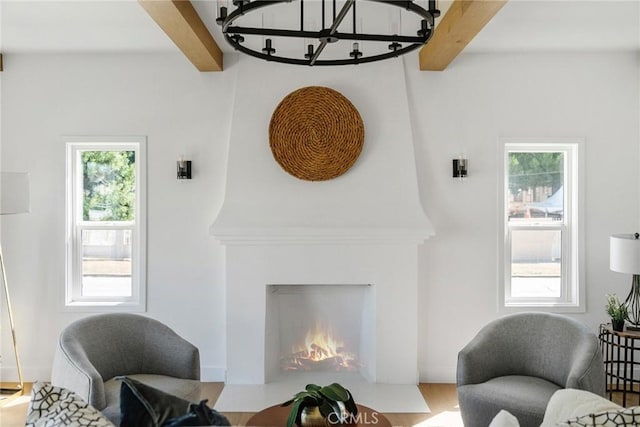 living area featuring beamed ceiling, a large fireplace, hardwood / wood-style floors, and an inviting chandelier