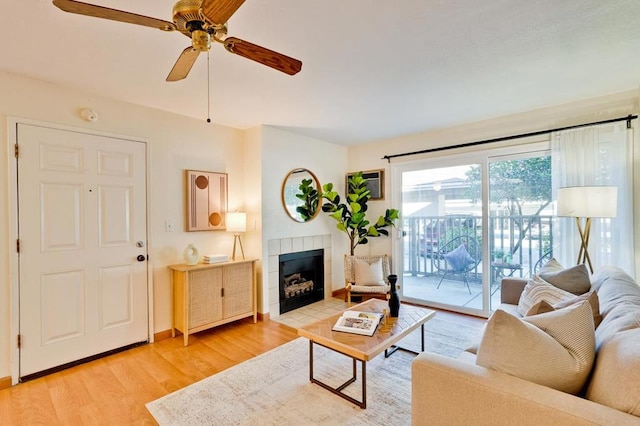 living room featuring ceiling fan, a tile fireplace, and wood-type flooring