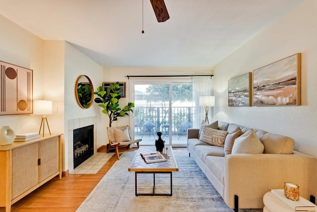 living room featuring ceiling fan, a tile fireplace, and light hardwood / wood-style flooring