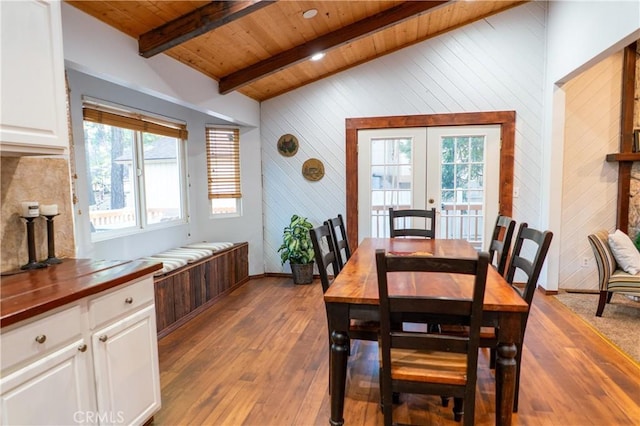 dining space featuring lofted ceiling with beams, a wealth of natural light, wood ceiling, and wood walls