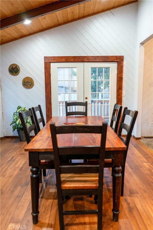 dining room featuring wood ceiling, wooden walls, wood-type flooring, lofted ceiling with beams, and french doors