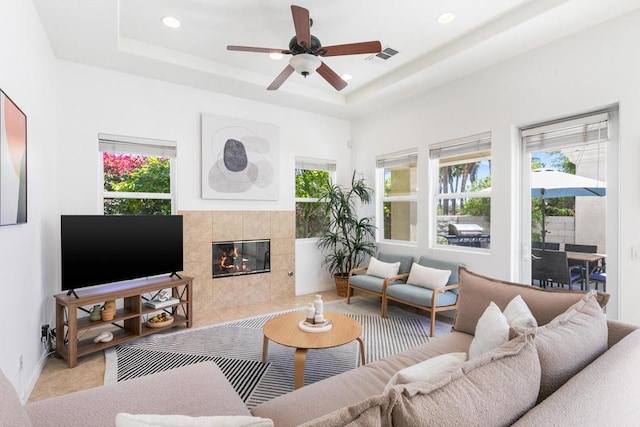 living room featuring ceiling fan, plenty of natural light, a tray ceiling, and a fireplace