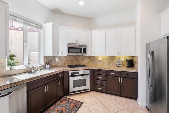 kitchen featuring light stone countertops, appliances with stainless steel finishes, sink, light tile patterned floors, and dark brown cabinets