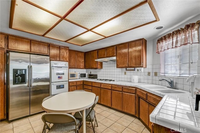 kitchen with sink, tasteful backsplash, tile countertops, white appliances, and light tile patterned floors