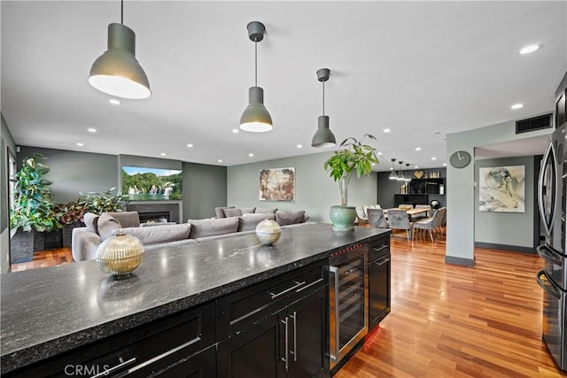 kitchen featuring pendant lighting, dark stone countertops, beverage cooler, and light hardwood / wood-style flooring