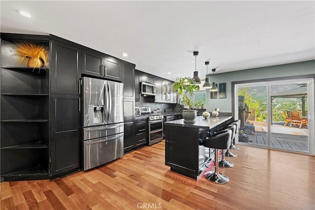 kitchen with a kitchen breakfast bar, hanging light fixtures, light hardwood / wood-style flooring, a kitchen island, and stainless steel appliances