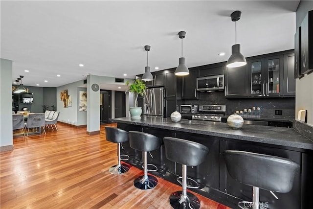 kitchen with a breakfast bar, backsplash, light hardwood / wood-style flooring, decorative light fixtures, and stainless steel appliances