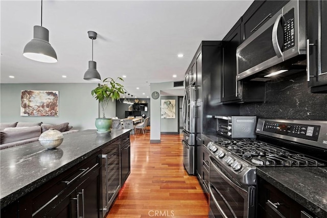 kitchen with dark stone counters, hanging light fixtures, decorative backsplash, appliances with stainless steel finishes, and light hardwood / wood-style floors