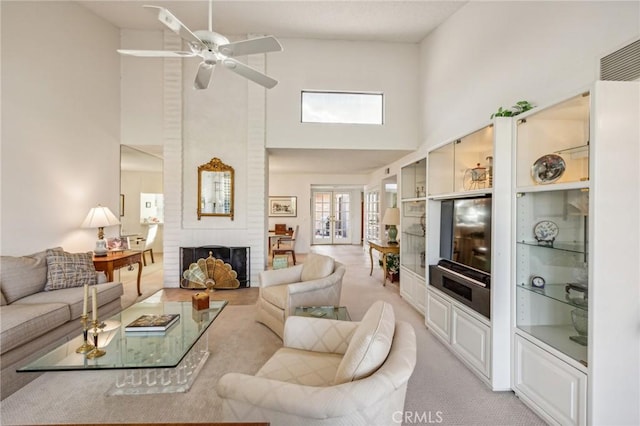 living room with french doors, a high ceiling, a brick fireplace, light carpet, and ceiling fan