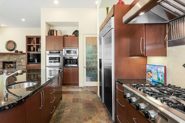 kitchen with built in appliances, sink, dark stone countertops, and extractor fan