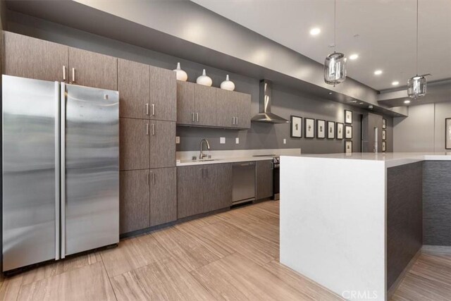 kitchen featuring decorative light fixtures, dark brown cabinets, sink, appliances with stainless steel finishes, and wall chimney exhaust hood