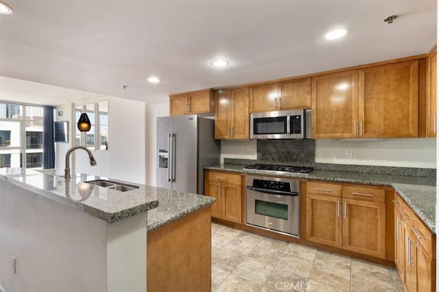 kitchen with sink, an island with sink, appliances with stainless steel finishes, and dark stone countertops