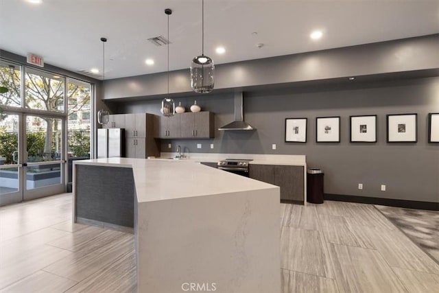 kitchen featuring decorative light fixtures, stainless steel appliances, a center island, and wall chimney range hood