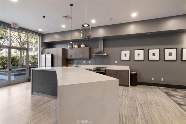 kitchen featuring decorative light fixtures, stainless steel appliances, a center island, and wall chimney range hood