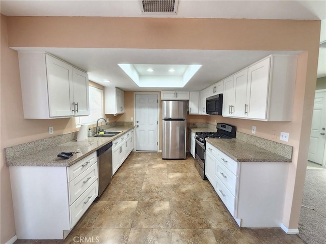 kitchen with a raised ceiling, sink, appliances with stainless steel finishes, light stone counters, and white cabinetry