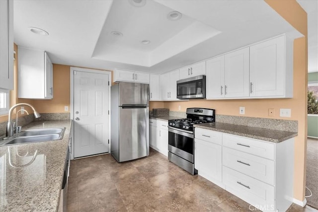 kitchen with a raised ceiling, white cabinetry, appliances with stainless steel finishes, and sink