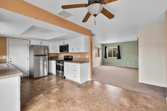 kitchen featuring ceiling fan, appliances with stainless steel finishes, white cabinetry, carpet flooring, and a tray ceiling