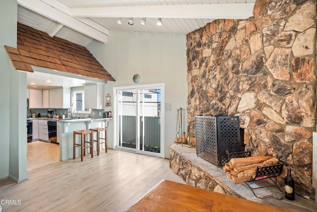 living room featuring a fireplace, vaulted ceiling with beams, light hardwood / wood-style flooring, and sink