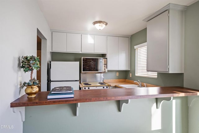 kitchen with white appliances, a kitchen breakfast bar, sink, kitchen peninsula, and white cabinetry