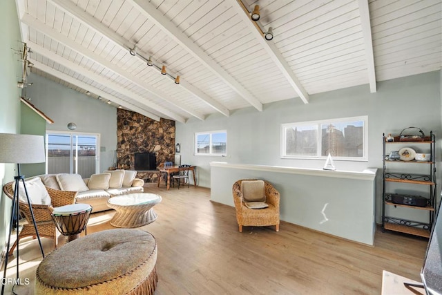 living room featuring beam ceiling, light wood-type flooring, a stone fireplace, and a healthy amount of sunlight